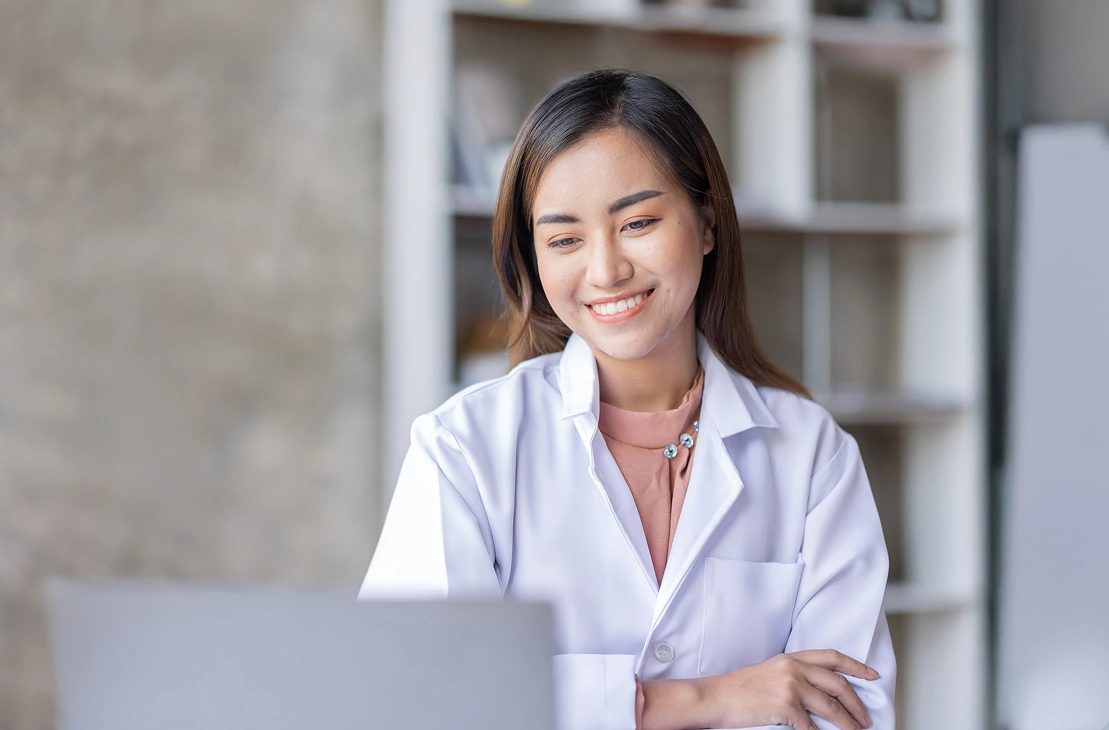 Smiling woman in a white coat using a laptop